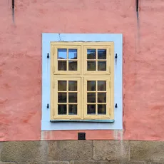 Three yellow-framed windows on a pink pastel wall with a stone foundation.