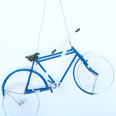 A blue vintage bicycle hanging on a white wall with its wheels parallel to the wall, creating a decorative display.