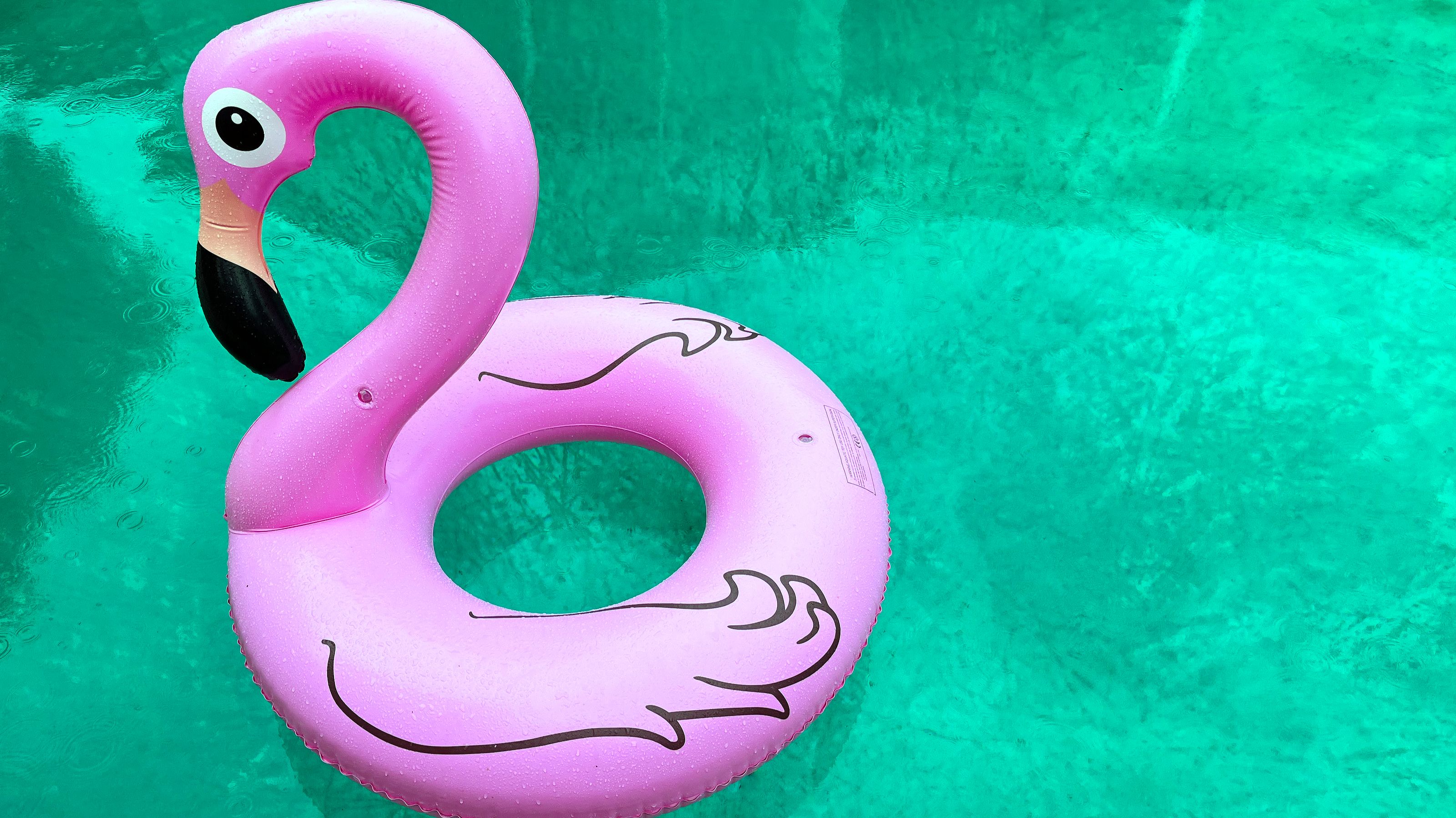 A pink flamingo pool float in bright turquoise water.