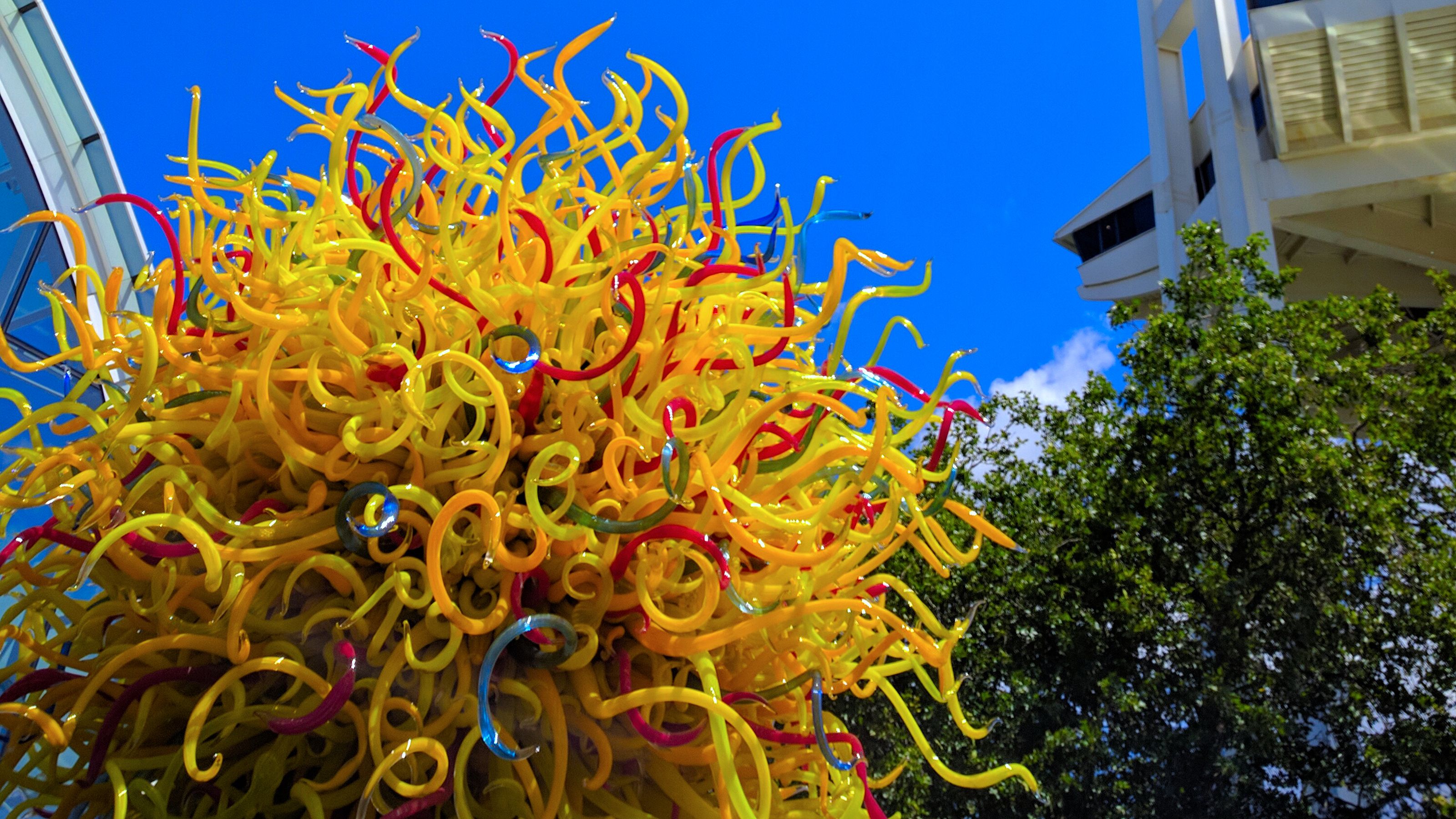 Vibrant glass sculpture with twisting yellow and red tendrils under a blue sky, adjacent to the Space Needle.