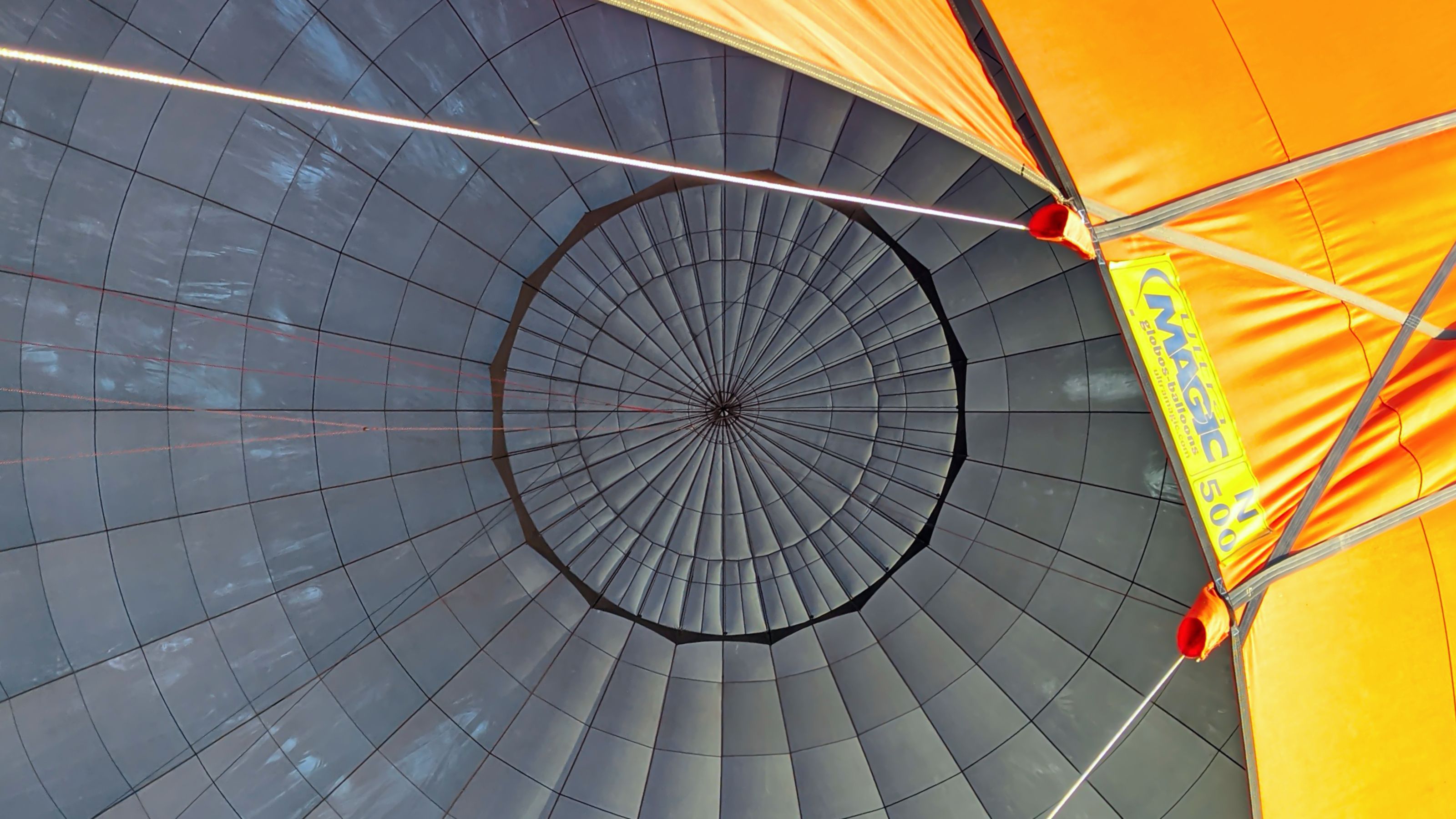 Interior view of a hot air balloon's vent, showcasing the geometric patterns and bright orange fabric.